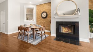 A dining area with a brick accent wall, a fireplace, and a round mirror above it. - 4BD Condo w/Parking & Game Room (Chicago)