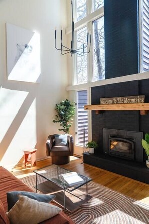 A modern living room with a fireplace, a sofa, a coffee table, and a large window allowing natural light.