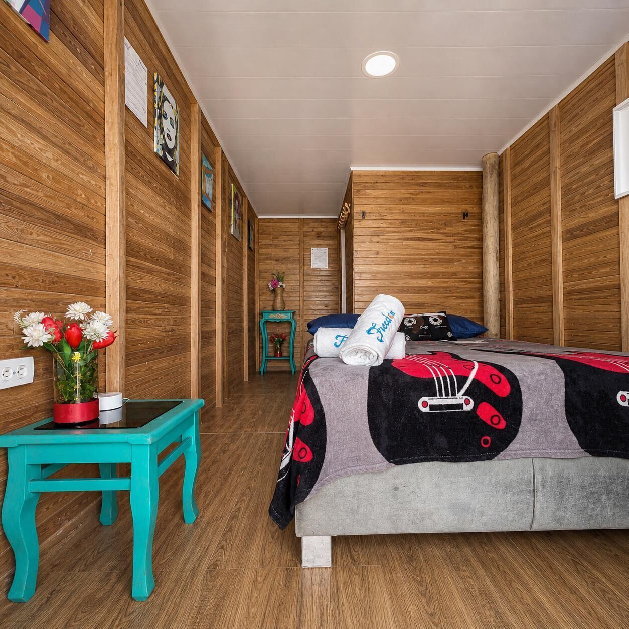 Een kamer met houten lambrisering, een bed, een kleine tafel met bloemen en een blauwgroene stoel.