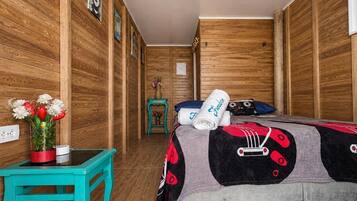 Een kamer met houten lambrisering, een bed, een kleine tafel met bloemen en een blauwgroene stoel.