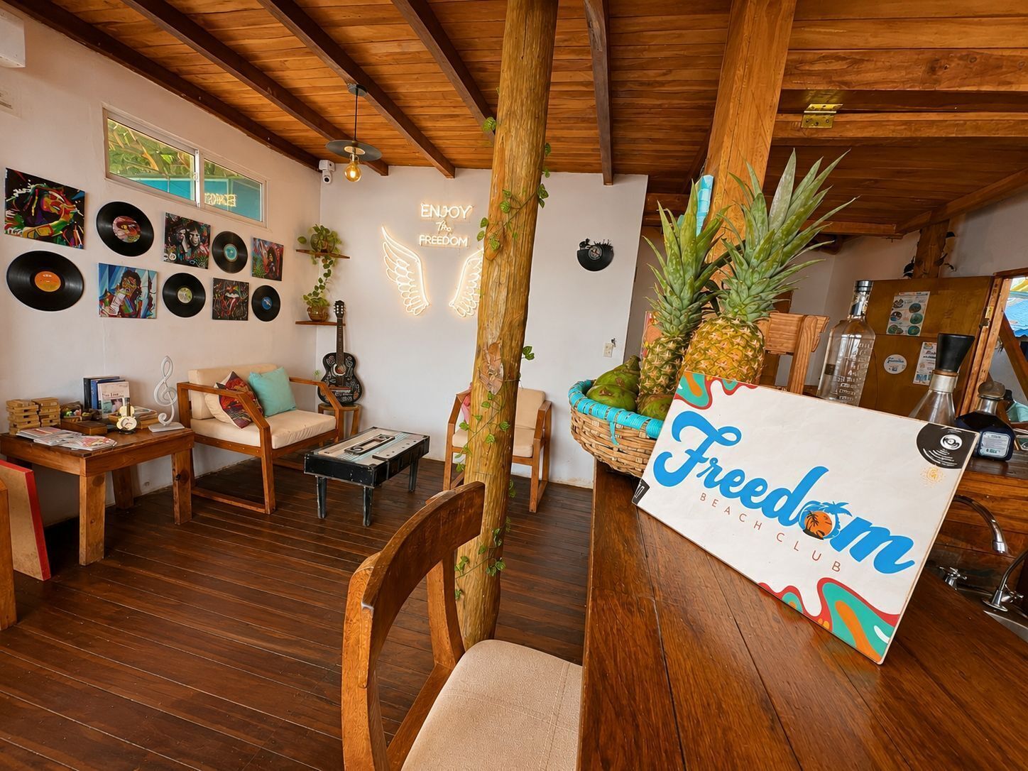 Uma sala de estar aconchegante com móveis de madeira, um violão e uma parede decorada com discos de vinil e um letreiro de neon.