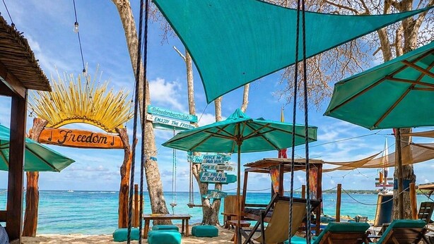 A beach setting with a swing chair, lounge chairs, and a sign reading 'Freedom.' - Freedom Beach Hotel (Cartagena)