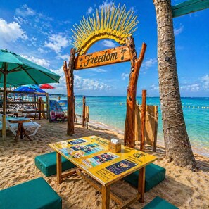 A beachside setup with a wooden arch labeled 'Freedom,' a table with brochures, and beach chairs under umbrellas. - Freedom Beach Hotel (Cartagena)