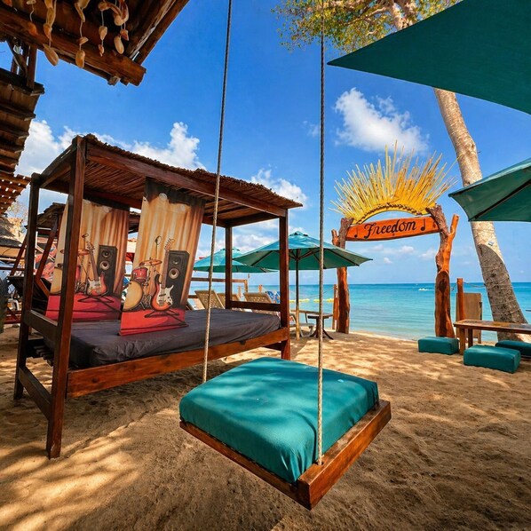 A beach cabana with a bed, a sign reading 'Freedom,' and a palm tree. - Freedom Beach Hotel (Cartagena)