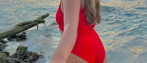 Une personne vêtue d’un maillot de bain rouge, se tenant la main avec une autre personne sur une plage, au coucher du soleil.