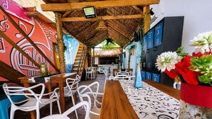 A restaurant with a wooden table, white chairs, a thatched roof, and colorful murals. - Freedom Beach Hotel (Cartagena)