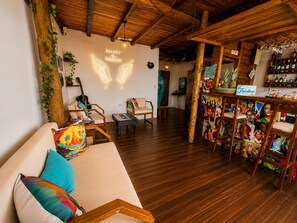 A wooden interior with a sofa, chairs, a bar area, and a neon sign. - Freedom Beach Hotel (Cartagena)