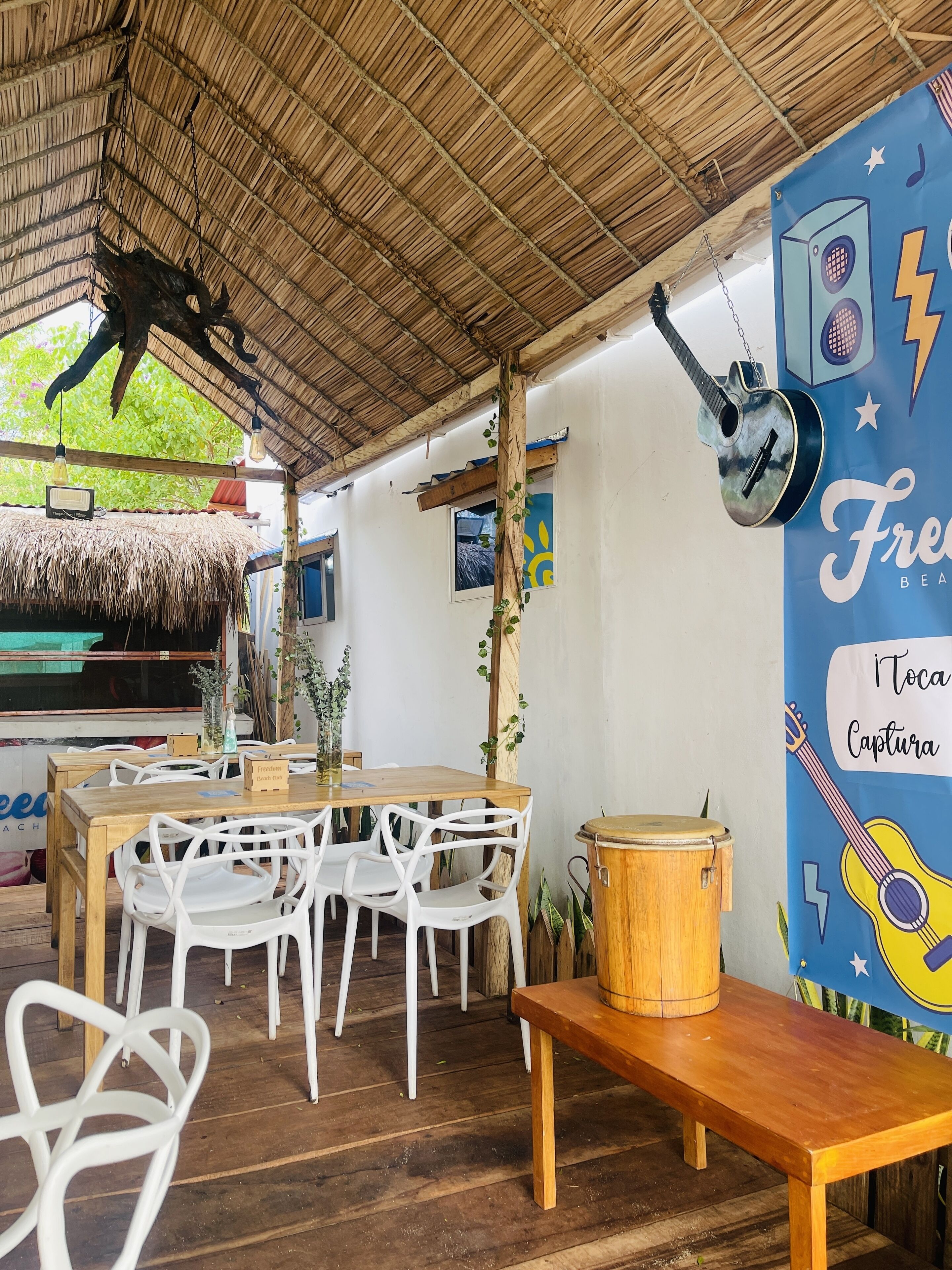 Un espace de restauration en plein air avec des tables et des chaises en bois, un toit de chaume et une fresque représentant des instruments de musique.