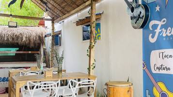 Un espace de restauration en plein air avec des tables et des chaises en bois, un toit de chaume et une fresque représentant des instruments de musique.