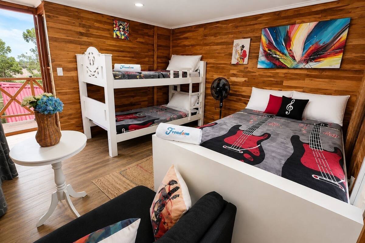 A room with bunk beds, a bed with a guitar-themed bedspread, a fan, and a table with a vase of flowers.