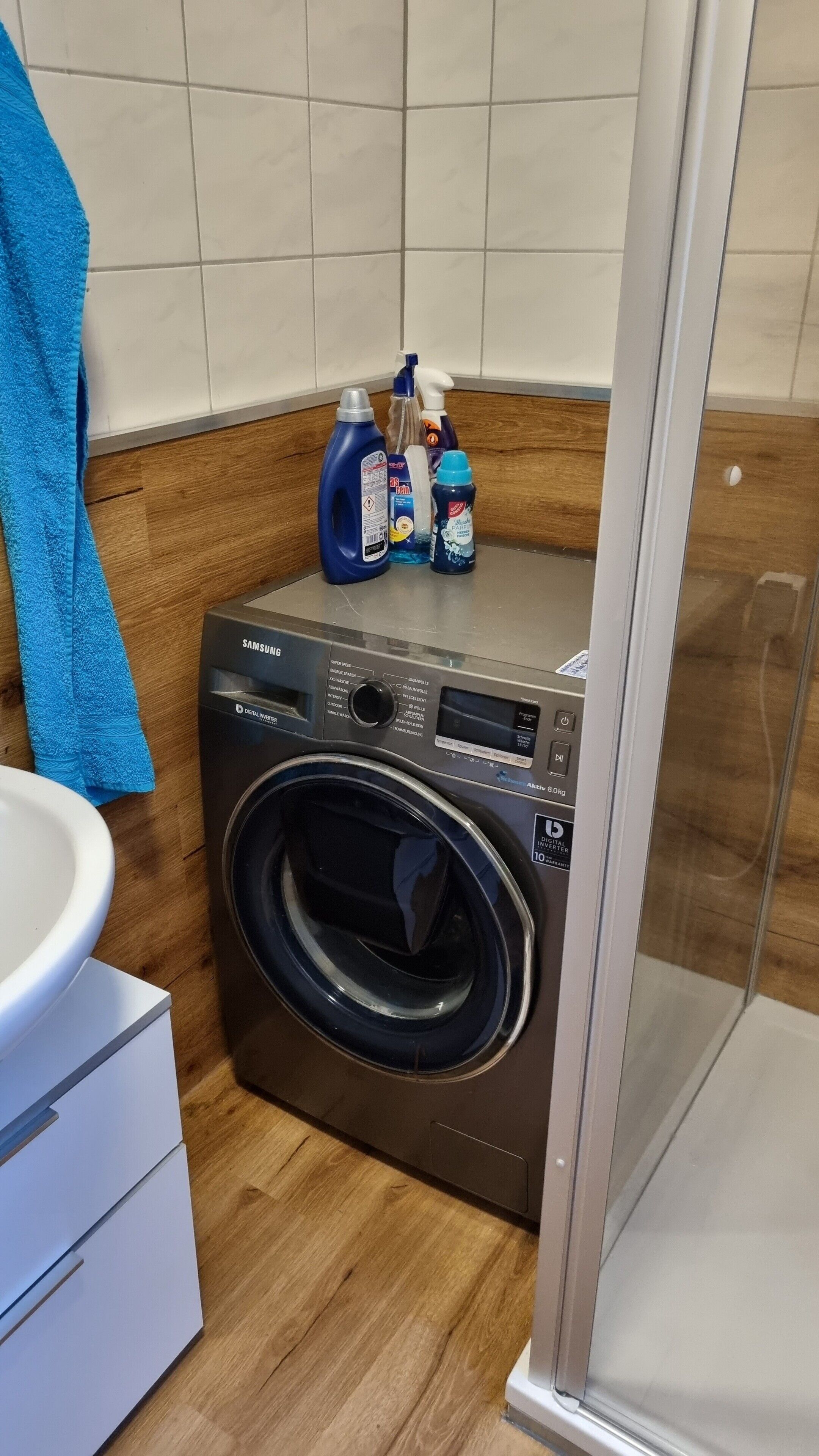 Una lavadora Samsung con inversor digital, una botella de detergente azul y un pulverizador encima.