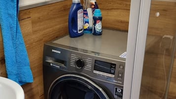 Una lavadora Samsung con inversor digital, una botella de detergente azul y un pulverizador encima.