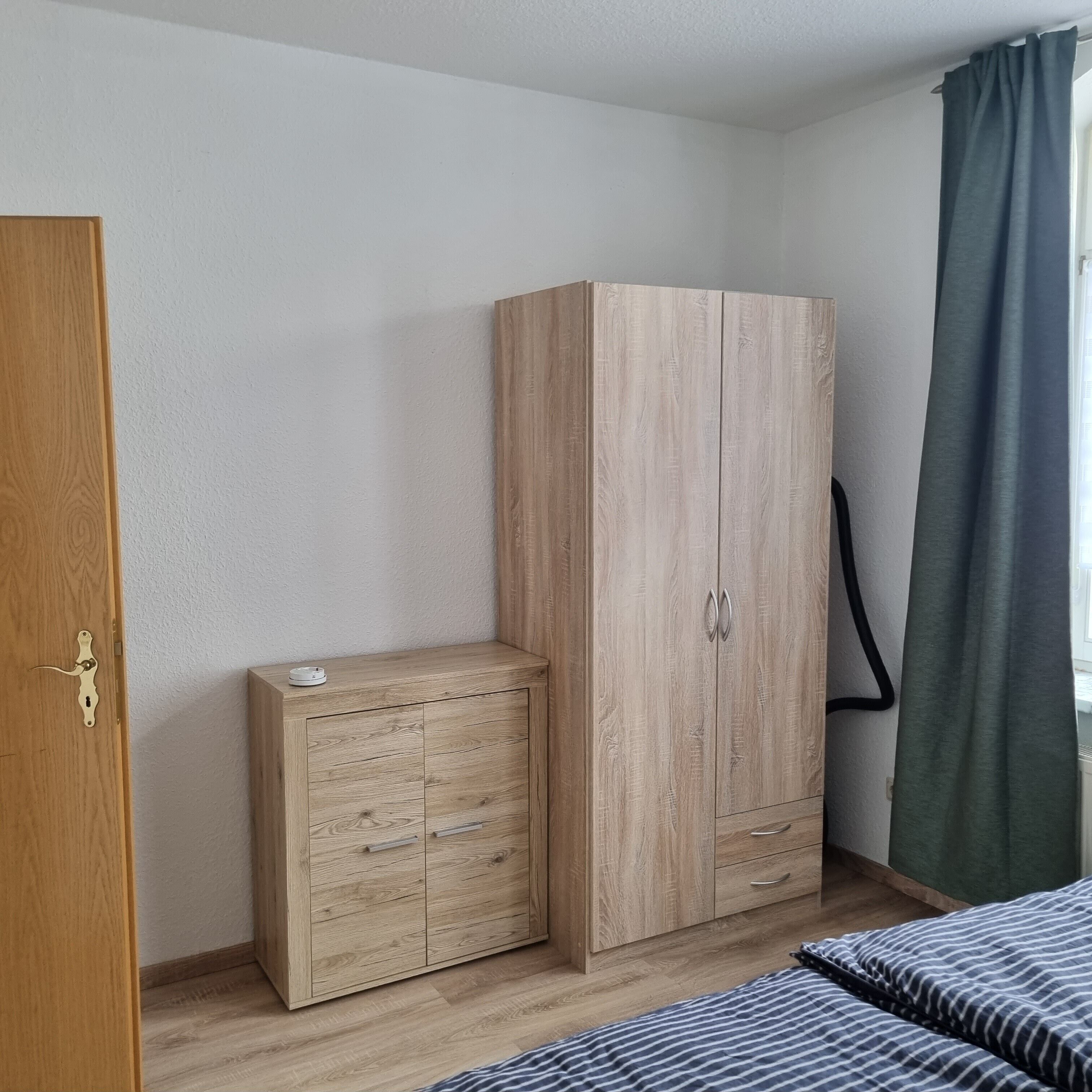 Una habitación con un armario de madera, una mesita de noche pequeña y una cama con ropa de cama a rayas.