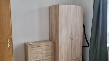 Una habitación con un armario de madera, una mesita de noche pequeña y una cama con ropa de cama a rayas.