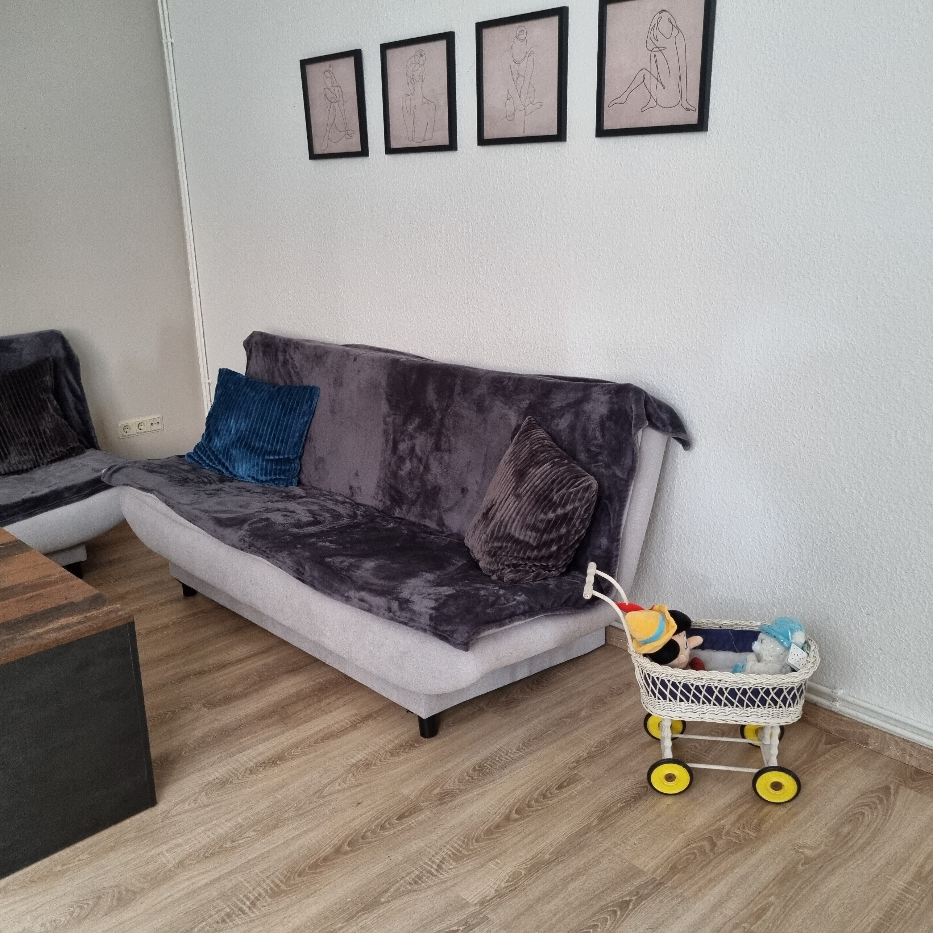 Ein modernes Wohnzimmer mit einem grauen Sofa, einem blauen Kissen und einem Kinderwagen mit Spielzeug.