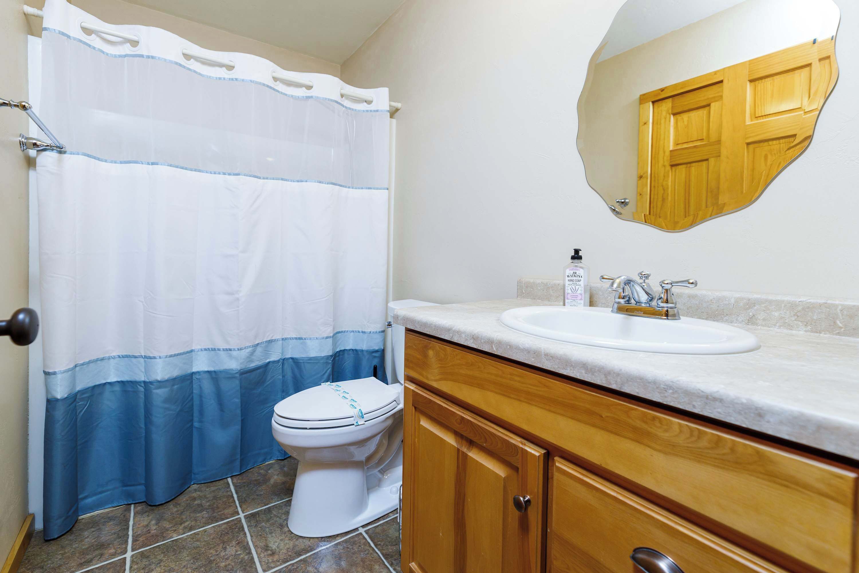Un baño con cortina de ducha, inodoro, lavabo, armarios de madera y un espejo.
