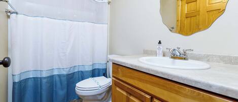 Un baño con cortina de ducha, inodoro, lavabo, armarios de madera y un espejo.