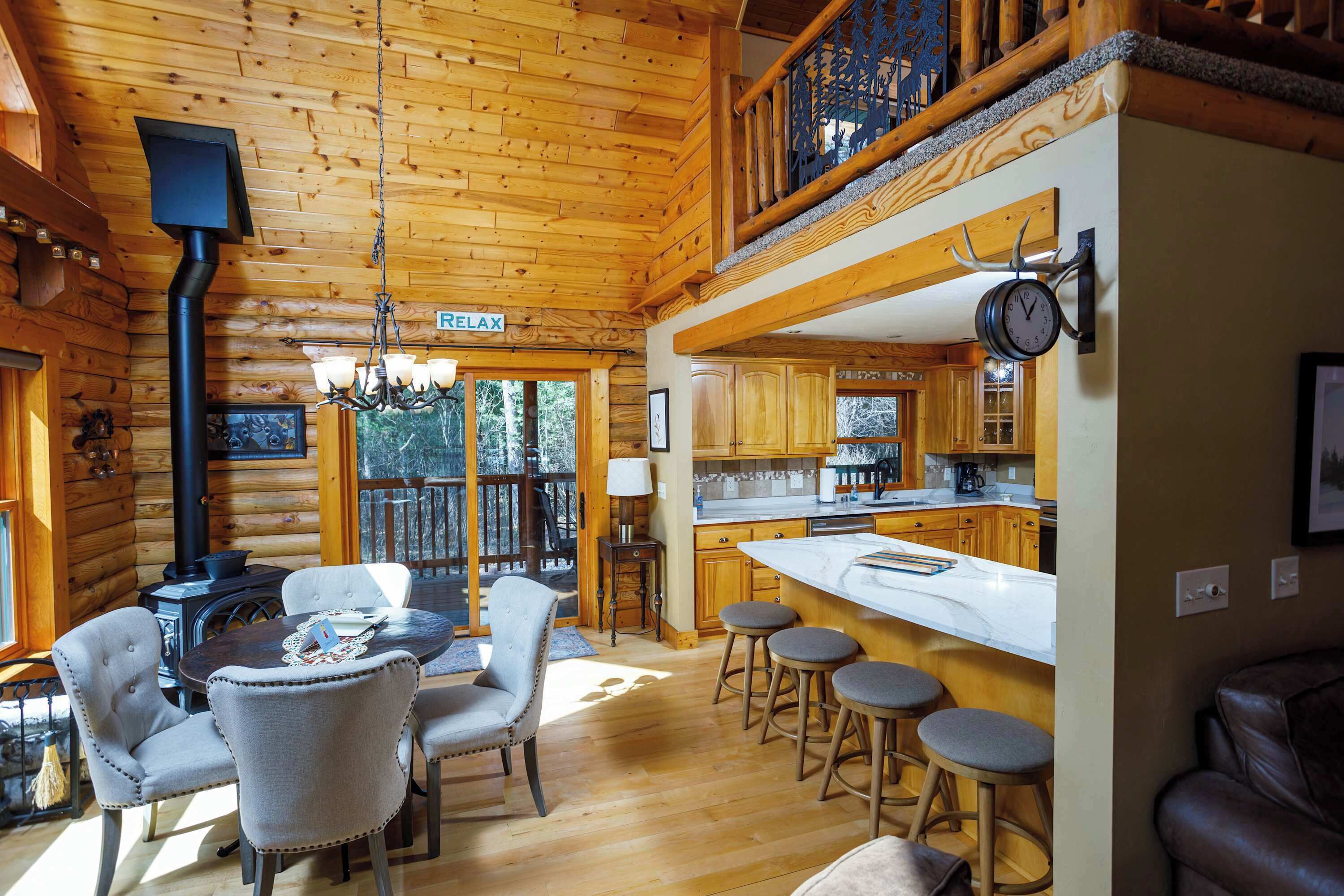 A log cabin interior with a dining area, kitchen, and a staircase leading to a loft.