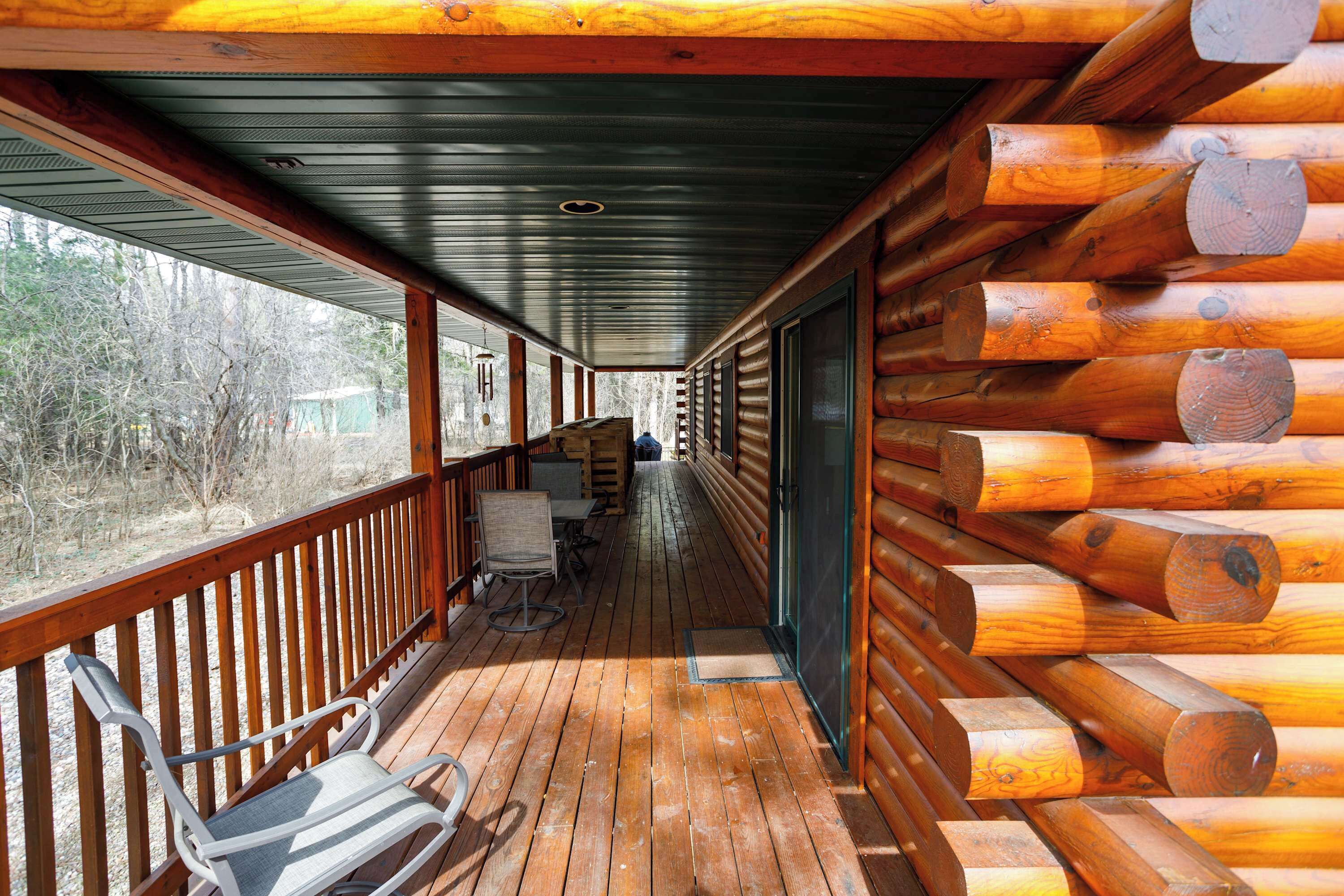 A covered wooden deck with a bench and table, surrounded by log walls.