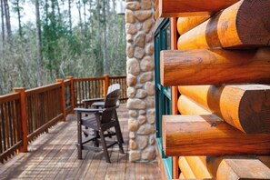 A wooden deck with a stone wall, wooden railing, and a rocking chair.