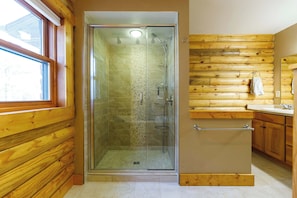 A bathroom with a glass-enclosed shower, wooden walls, a sink, and a towel rack.