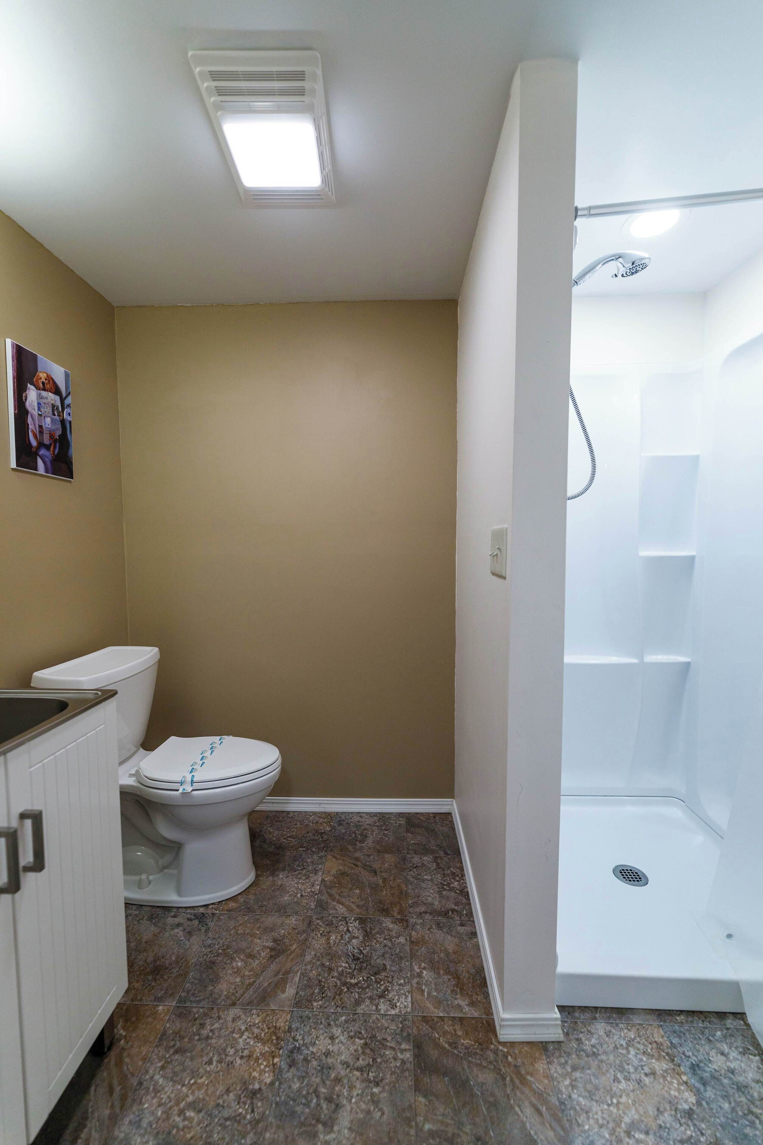 A bathroom with a toilet, shower, and a light fixture on the ceiling.