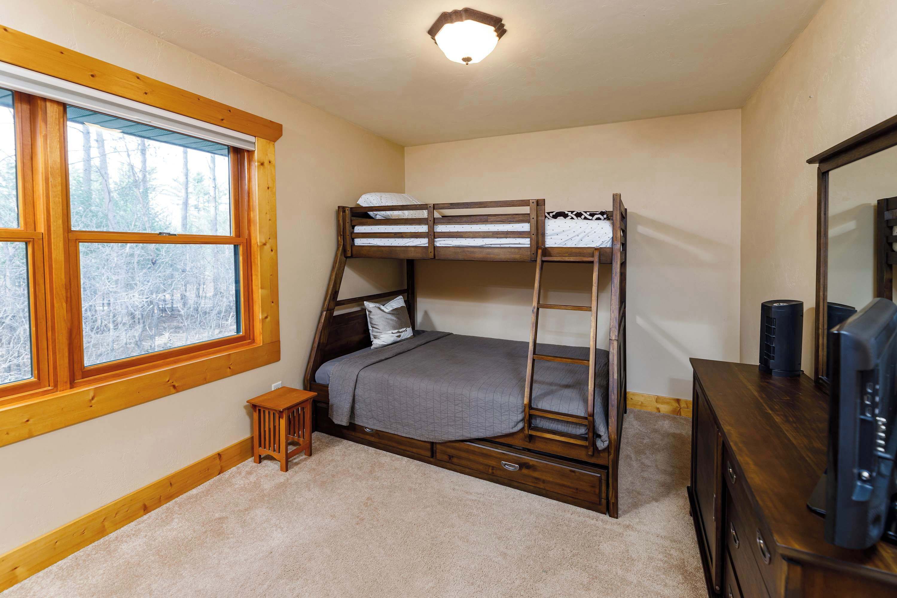 A bunk bed with a ladder, a small wooden stool, a dresser, and a television.