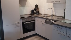 A compact kitchen with a built-in oven, a coffee maker, and a stainless steel sink. - Holiday Apartment "Lila Pause" with Private Terrace & Wi-Fi (Ellweiler)