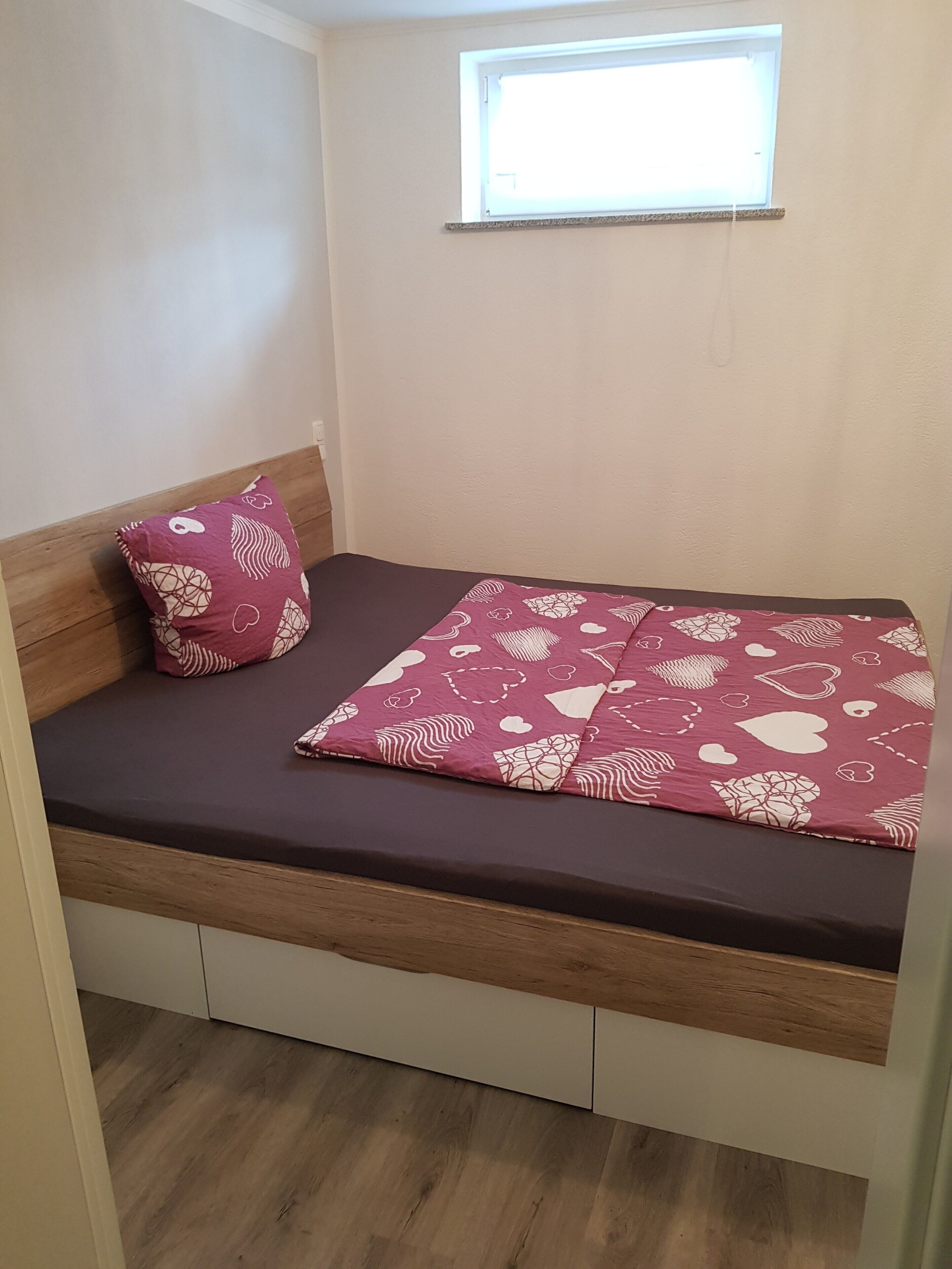 Un petit lit avec une couvre-lit à motifs, un oreiller et une fenêtre au-dessus.