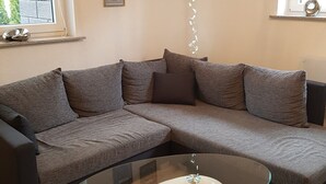 A modern living room with a sectional sofa, a glass coffee table, and a hanging light fixture. - Holiday Apartment "Lila Pause" with Private Terrace & Wi-Fi (Ellweiler)