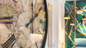 Un reloj de pared grande con un mapa, una lámpara moderna y una silla azul.