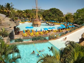A large outdoor swimming pool with a ship-shaped slide, surrounded by palm trees and yellow lounge chairs.