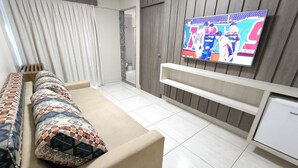 Quarto de hotel moderno com sofá, TV e pequena cozinha.