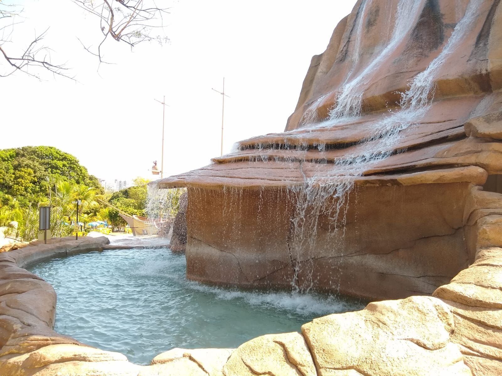 A rock waterfall feature with a pool at its base, surrounded by large boulders and greenery.