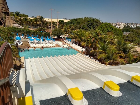 Eine Wasserrutsche, die in einen Pool mit Palmen und Liegestühlen mündet.