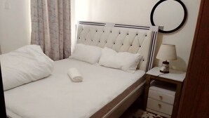 A neatly made bed with white linens and pillows, a bedside table with a lamp, and a cowhide rug on the floor. - 1 Bed Flat Sleeps 2 with On-Site Parking (Nairobi)