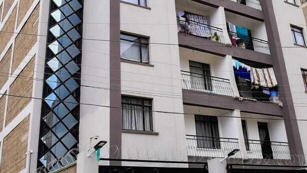 A multi-story residential building with balconies, a garage, and a white car parked in front. - 1 Bed Flat Sleeps 2 with On-Site Parking (Nairobi)