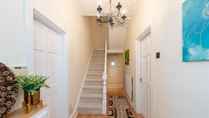 A hallway with a staircase, a chandelier, a wooden floor, and a patterned rug.