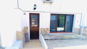 Un bâtiment à l’extérieur blanc, avec une porte en bois et une grande porte-fenêtre coulissante.