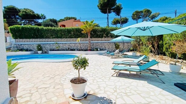 Un espace piscine agrémenté de chaises longues et de parasols, entouré d’une terrasse en pierre et de verdure.
