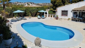Une piscine entourée de chaises longues et de parasols, agrémentée de plantes en pot et offrant une vue sur une colline.
