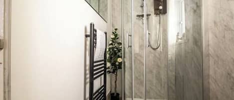 Un baño moderno con cabina de ducha de vidrio, paredes de mármol y suelo de madera.
