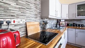 A modern kitchen with a wood countertop, a black induction cooktop, and white cabinets. - The Boat House Sleeps 4 Pet Friendly (Dawlish)