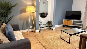 Ein Wohnzimmer mit einer Couch, einem Couchtisch, einem Fernseher, einer Lampe und einer Pflanze.