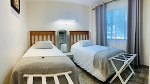 A twin room with two beds, a small table, a mirror, and a window with curtains. - Mispa George - Self Catering Apartment - Sleeps 2 (George)