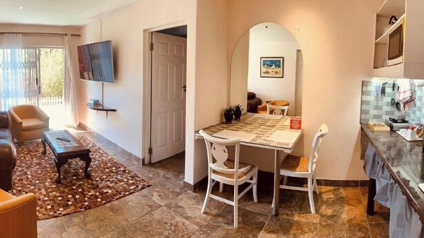 A living room with a sofa, armchair, and coffee table, a dining area with a table and chairs, and a kitchen with a microwave and cabinets. - Mispa George - Self Catering Apartment - Sleeps 2 (George)