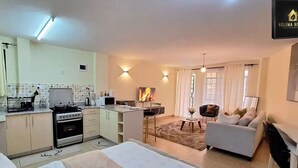Een compact woongedeelte met een kitchenette, een eethoek en een zithoek met een bank en stoelen.