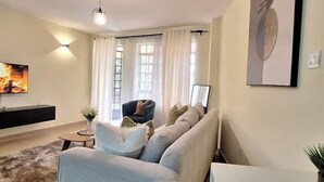 Een moderne woonkamer met een bank, salontafel, televisie en een groot raam met gordijnen.
