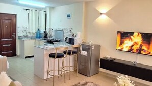 Een moderne keuken met een centraal eiland, barstoelen, een koelkast en een flatscreen televisie aan de muur.