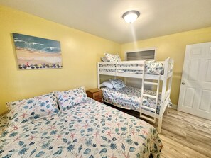 Een kamer met een stapelbed, een enkel bed, een schilderij van een strandgezicht en een deur.